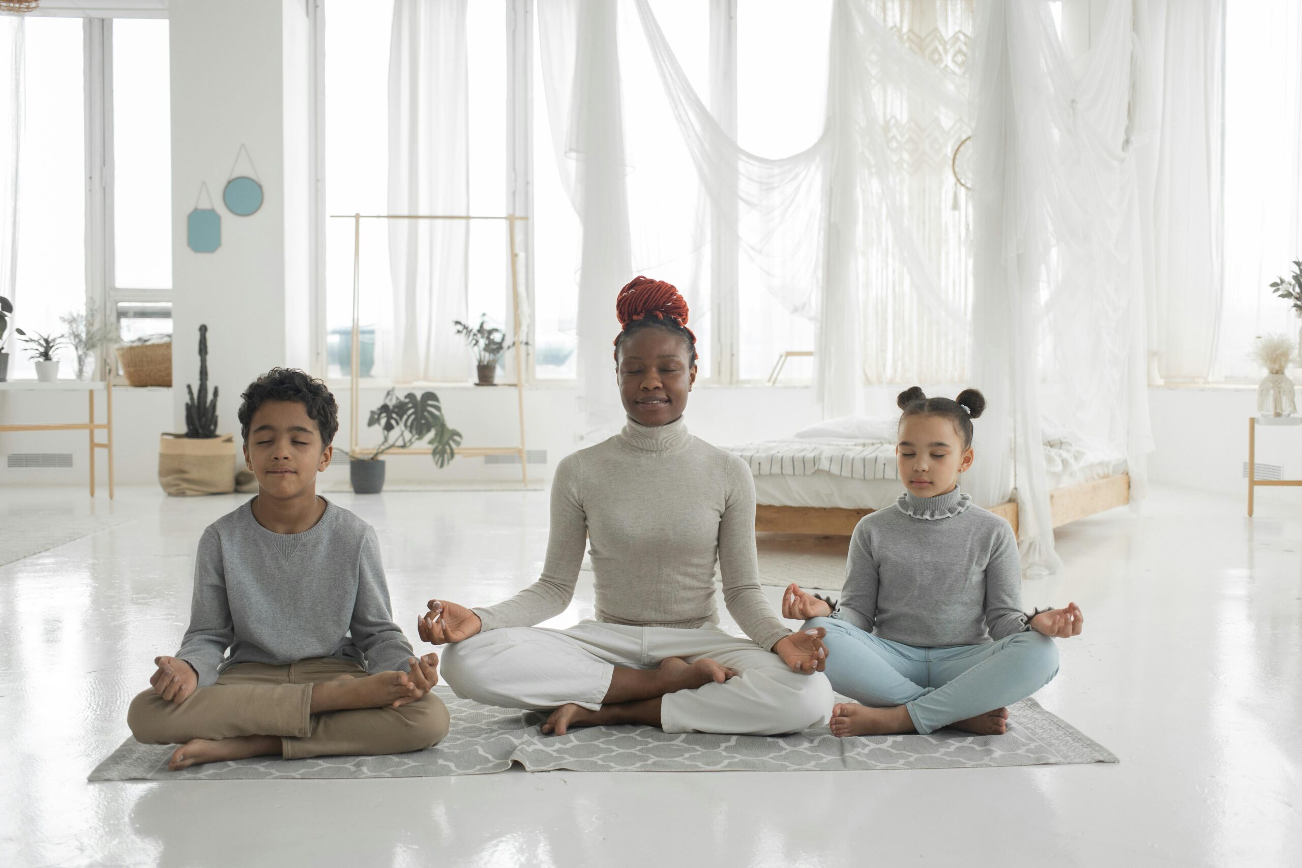 a woman and two children sitting in a yoga pose in a bedroom