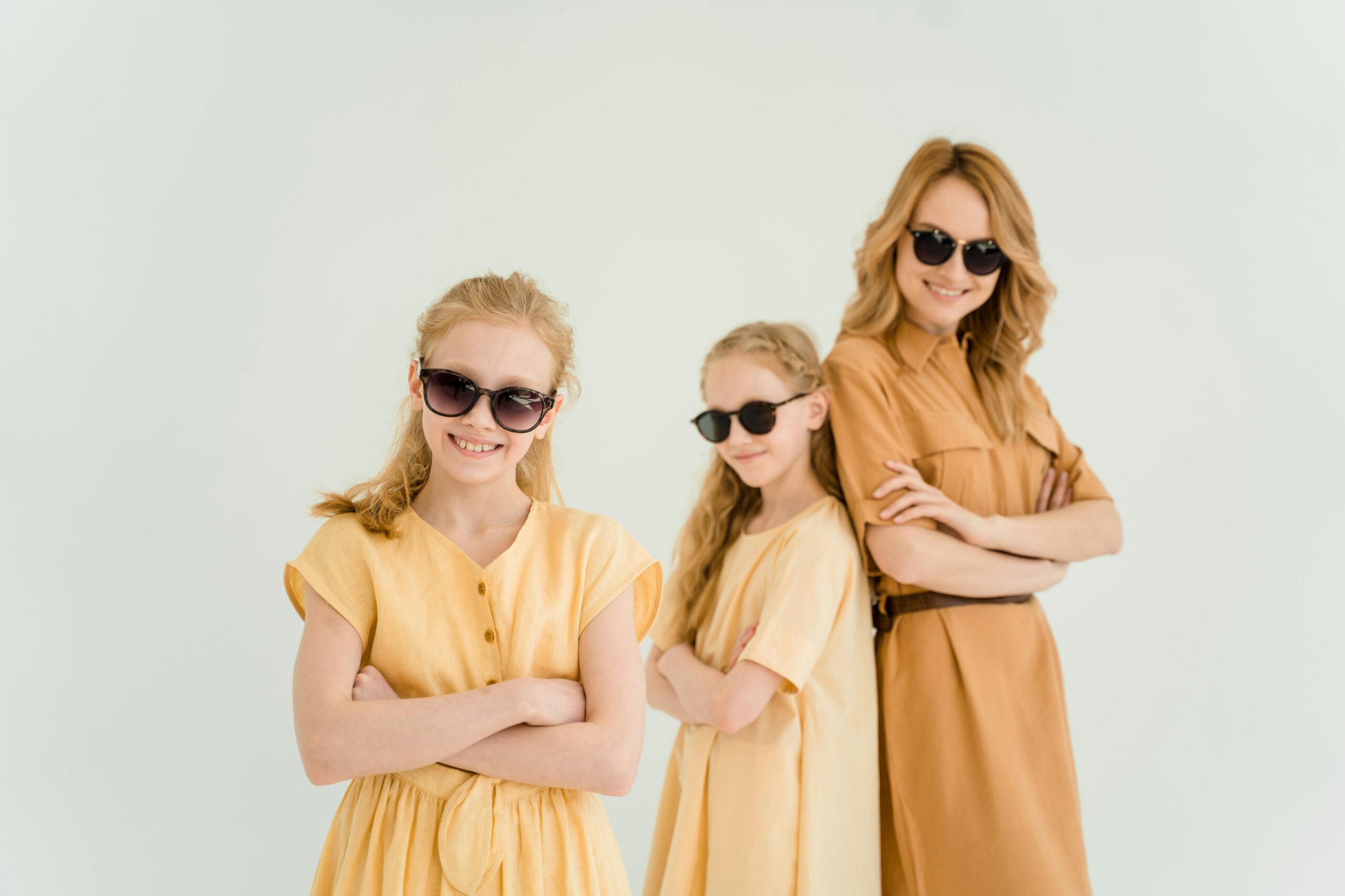 a mom and her two girls wearing yellow dresses and posing with their arms crossed