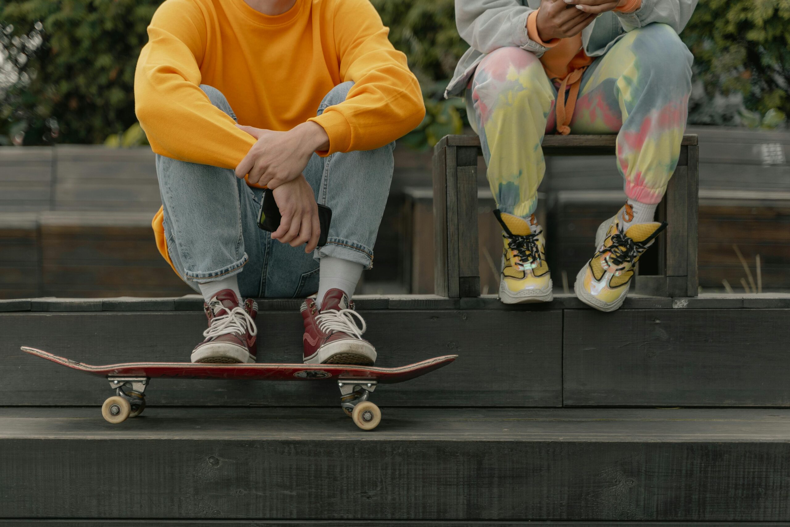 two teens sitting on a ledge with a skateboard